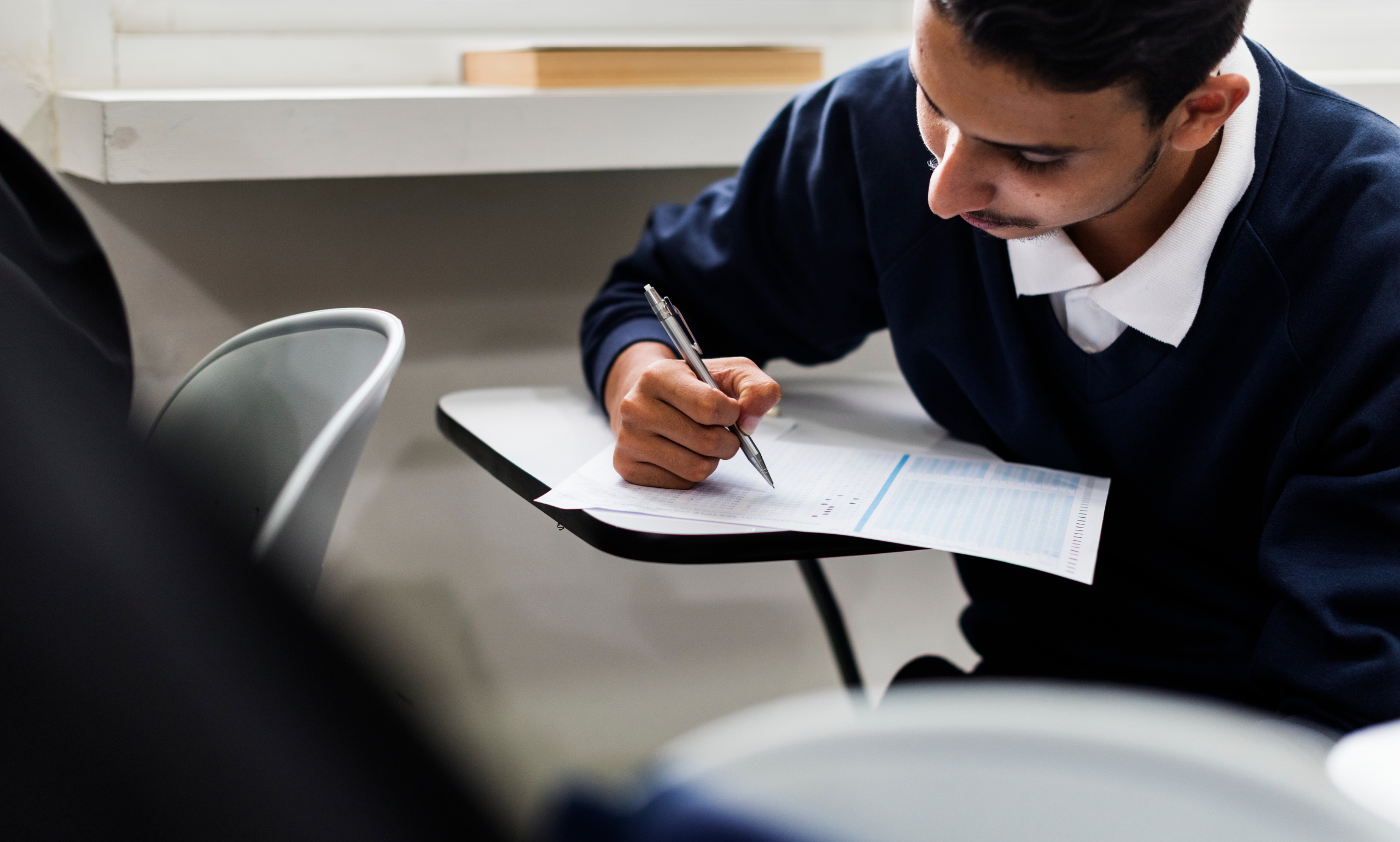 A focused student taking a traditional written exam in a classroom setting