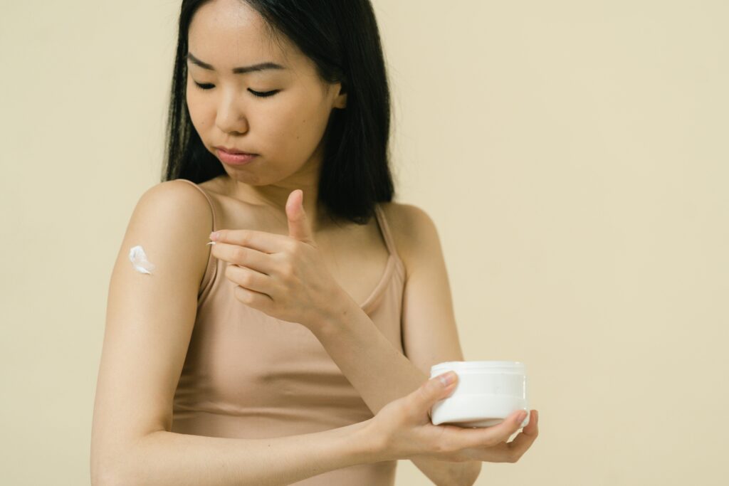 A young woman applying clean beauty moisturizer cream on her face as part of her natural skincare routine